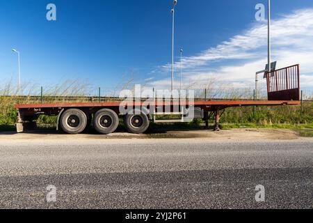 Ein leerer roter Anhänger steht am Straßenrand, mit blauem Himmel und hellen Wolken im Hintergrund Stockfoto