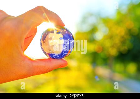 Hand mit einem kugelförmigen Puzzleteil, das von Sonnenlicht beleuchtet wird, vor einem natürlichen Hintergrund mit weichem Fokus. Nachhaltige Zukunft für die Erde. Stockfoto