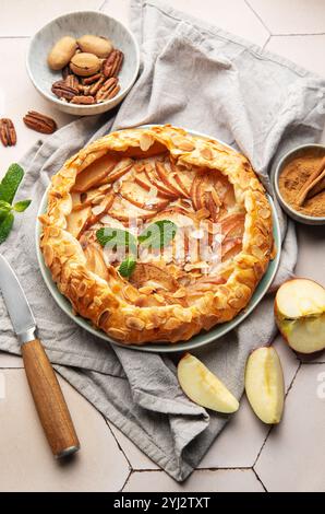 Frisch gebackene Apfelgalette, dekoriert mit Mandelflocken, Minzblättern, Zimt und Pekannüssen, serviert auf Keramikplatte Stockfoto