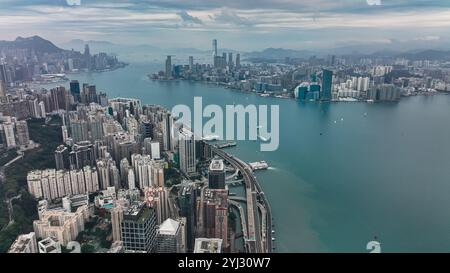 Ein fantastischer Blick auf die Victoria Bay, die pulsierende Skyline von Hongkong und die geschäftige Aktivität am Wasser unter einem bewölkten Himmel. Stockfoto