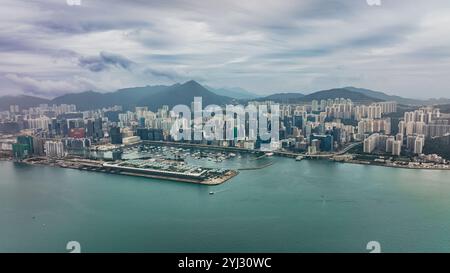 Der Blick fängt Victoria Bay mit einer geschäftigen Skyline, hoch aufragenden Gebäuden und Bergen im Hintergrund ein, die die urbane Landschaft von Hongkong widerspiegeln. Stockfoto