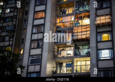 Beleuchtete Fenster von Wohngebäuden in Hongkong zeigen tagsüber Aktivitäten des täglichen Lebens während des Abends, während Kleidung zum Trocknen draußen hängt. Stockfoto
