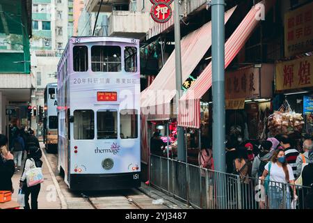 Eine Straßenbahn fährt durch die überfüllte Hong Kong Market Station, wo Käufer lebhafte Verkaufsstände und Straßenverkäufer erkunden. Stockfoto