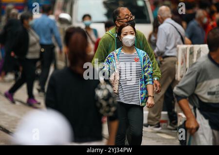 Fußgänger laufen durch eine belebte Straße im Zentrum von Hongkong, viele tragen Masken, während sie ihre täglichen Aktivitäten ausführen. Stockfoto