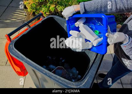 Person, die leere Plastikflaschen und Lebensmittelverpackungen aus Metall in einen Recyclingbehälter kippt Stockfoto