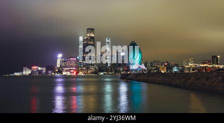 Die Skyline von Hongkong leuchtet nachts hell und bietet moderne Architektur und bunte Lichter, die sich auf dem Wasser spiegeln. Stockfoto