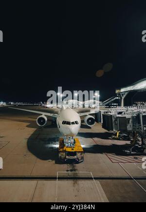 Ein großes Flugzeug parkt an einem Gate in Hongkong, wobei die Bodenbesatzung es für den nächsten Flug unter hellen Terminallichtern vorbereitet. Stockfoto