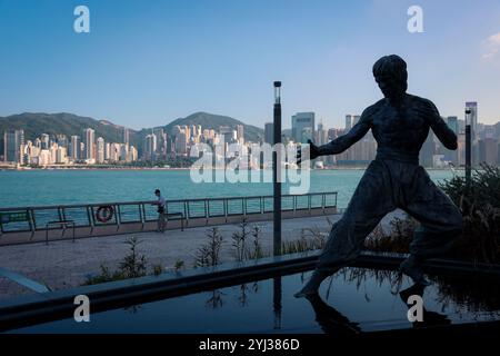 Eine Bronzestatue von Bruce Lee steht stolz am Ufer mit Blick auf die geschäftige Skyline der Stadt und das ruhige Wasser von Hongkong. Stockfoto