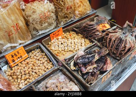 Lebendige Auswahl an getrockneten Meeresfrüchten, die in Holzkisten auf einem Markt in Hongkong präsentiert werden und im Morgenlicht mit einheimischen Käufern zu tun haben. Stockfoto