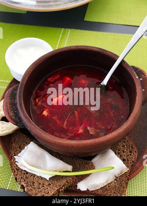 Eine lebendige und herzhafte Schüssel mit traditioneller Borschtsuppe, serviert in einem rustikalen Tontopf, begleitet von Scheiben Roggenbrot und einer Seite Sauerrahm. Perfec Stockfoto