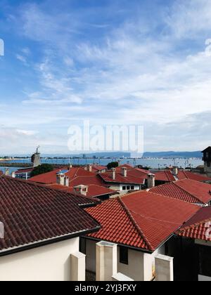 Dieses Bild zeigt eine malerische Aussicht auf mehrere rote Dächer unter einem wunderschönen blauen Himmel, mit einem ruhigen Meer im Hintergrund, das ein Gefühl für verkörpert Stockfoto