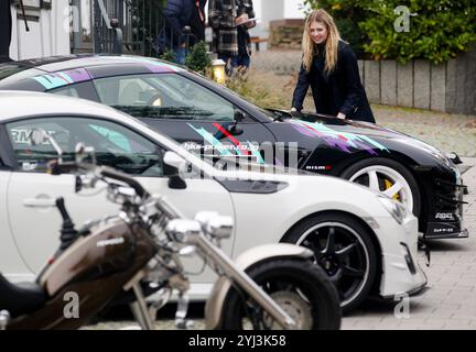 Essen, Deutschland. November 2024. Ein Modell sieht getunte Autos und ein Trike von Rewaco bei der Vorschau der Motorsport- und Tuningmesse Essen Motor Show. Rund 500 Aussteller aus 15 Ländern präsentieren auf der Automobilmesse ab 29.11 alles rund um Autos. Bis 8.12.2024. Vermerk: Roland Weihrauch/dpa/Alamy Live News Stockfoto