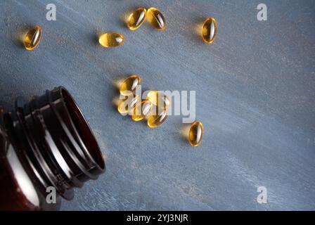 Omega-3 Fischöl Kapseln und Flaschen verstreut auf blauem Hintergrund, die Gesundheit und Wellness hervorheben. Stockfoto