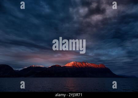 Bei Sonnenuntergang leuchtet die untergehende Sonne rot über den Bergen des Antarctic Sound, King Christian X Land, Nordost-Grönland-Nationalpark. Stockfoto