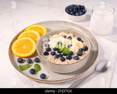 Gesunde Haferflocken über Nacht mit Banane, Heidelbeeren und einem Minzzweig mit Orangenscheiben an der Seite Stockfoto