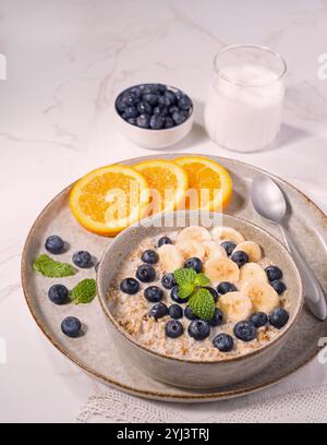Gesunde Haferflocken über Nacht mit Banane, Heidelbeeren und einem Minzzweig mit Orangenscheiben an der Seite Stockfoto
