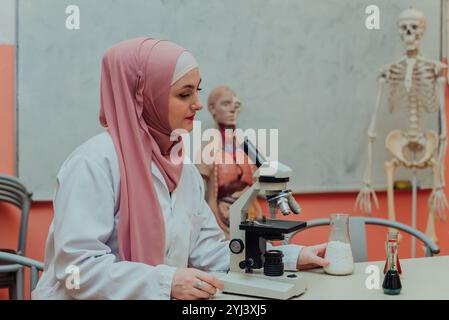 Eine weibliche muslimische Wissenschaftlerin, die wissenschaftliche Forschung macht und durch ein Mikroskop im Labor schaut. Stockfoto