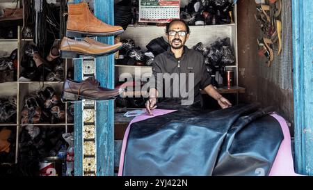 Ein nepalesischer Schuster in seinem Geschäft in Kathmandu, umgeben von handgefertigten Lederschuhen, die traditionelle Handwerkskunst und Hingabe an Qualität zeigen. Stockfoto