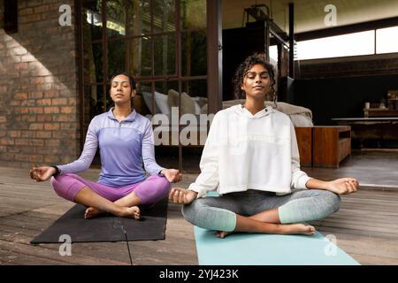 Multirassische Freundinnen üben Yoga auf Matten zu Hause und meditieren mit geschlossenen Augen Stockfoto