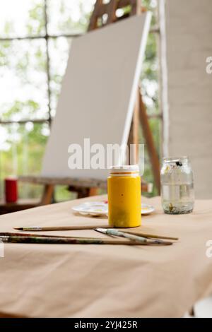 Gelbe Farbe und Pinsel auf dem Tisch im Kunststudio mit leerer Leinwand, zu Hause Stockfoto