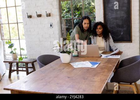 Zwei multirassische Freundinnen arbeiten zu Hause am Laptop zusammen und diskutieren über Dokumente und Ideen Stockfoto