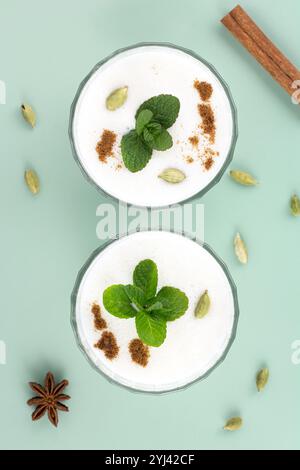 Traditionelles indisches kaltes Getränk Lassi in einem Glas mit Gewürzen und Minze auf grünem Hintergrund. Draufsicht. Stockfoto