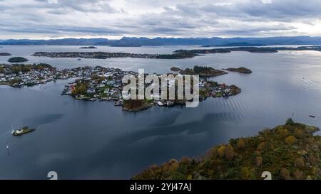 Aus der Vogelperspektive auf ein Küstendorf mit Häusern auf kleinen Inseln, umgeben von ruhigem Wasser und fernen Bergen unter einem bewölkten Himmel. Stockfoto