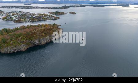 Aus der Vogelperspektive einer Fähre, die durch einen ruhigen Fjord fährt, umgeben von felsigen Inseln und einer Küstenstadt. Stockfoto