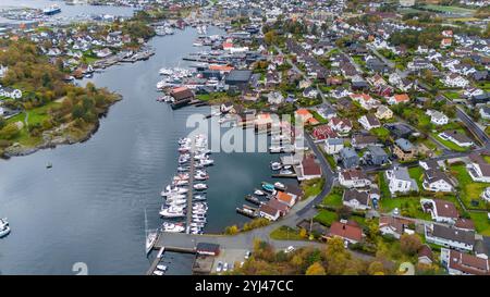 Aus der Vogelperspektive auf eine Küstenstadt mit einem Yachthafen voller Boote, umgeben von Wohnhäusern und Grün. Die Stadt liegt an einem gewundenen Wasser Stockfoto