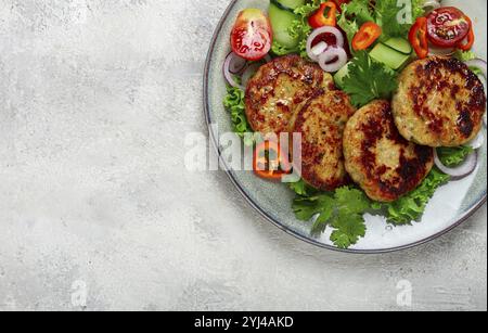 Gebratene Hähnchenkoteletts, gehacktes Hähnchen, mit Gemüse, auf Grau, mit Gemüsesalat, Aussicht von oben, hausgemacht, keine Leute Stockfoto