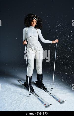 Eine atemberaubende brünette Afroamerikanerin modelliert einen eleganten Skianzug und strahlt Wintermode in Studioatmosphäre aus. Stockfoto