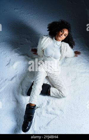 Eine modische Frau entspannt sich in einem weißen Skianzug und einer Kunstpelzjacke und genießt die verschneite Winteratmosphäre. Stockfoto