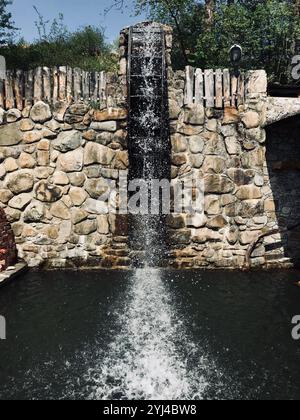 Ein rustikaler Stein-Wasserfall fällt wunderschön in einen friedlichen Teich, umgeben von natürlichem Grün in einer Umgebung im Freien, die eine ruhige und ruhige Atmosphäre schafft Stockfoto