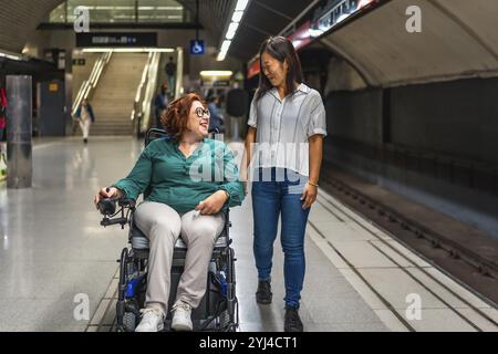 Frontalansicht einer glücklichen kaukasischen behinderten Frau und eines multiethnischen Freundes, der entlang der U-Bahn-Plattform spaziert Stockfoto