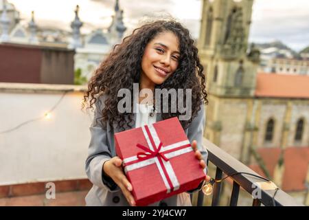 Porträt einer glücklichen hispanischen Frau, die ein Geburtstagsgeschenk auf einem Dach erhält Stockfoto