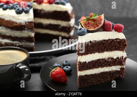 Ein Stück leckerer Schokoladen-Biskuitkuchen mit Beeren und Kaffee auf schwarzem Tisch, Nahaufnahme Stockfoto