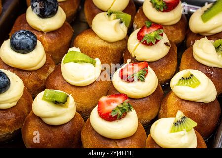 Verschiedene Cremepuffs mit frischen Früchten wie Kiwi, Erdbeeren und Heidelbeeren auf der Bäckerei Stockfoto