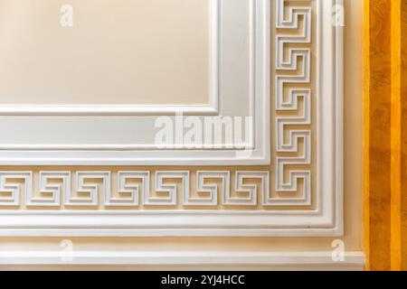 Dekorative Wandelemente mit weißem Meander-Motiv über gelbem Hintergrund, klassische antike Architekturvorlage, Hintergrundfotostruktur Stockfoto