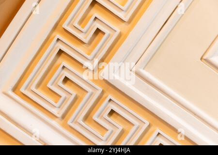 Klassische Wandelemente mit weißem Meander-Motiv über gelbem Hintergrund, antike Architekturvorlage, Hintergrundfotostruktur Stockfoto