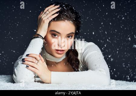 Eine umwerfende Frau liegt anmutig mit der Hand auf dem Kopf, umgeben von fallenden Schneeflocken. Stockfoto