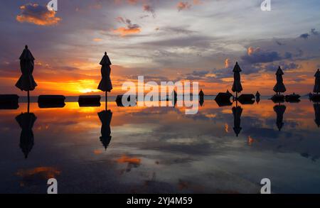 Geschlossene Sonnenschirme in einem Infinity-Pool mit Blick auf das Meer in einem dramatischen Sonnenuntergangshimmel Stockfoto