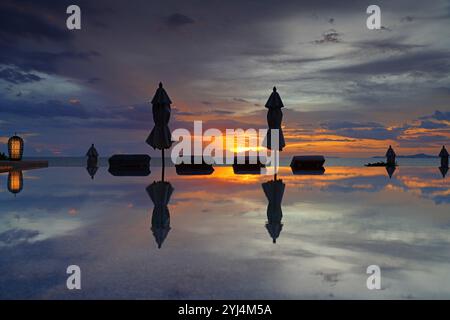 Geschlossene Sonnenschirme in einem Infinity-Pool mit Blick auf das Meer in einem dramatischen Sonnenuntergangshimmel Stockfoto