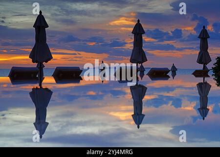 Geschlossene Sonnenschirme in einem Infinity-Pool mit Blick auf das Meer in einem dramatischen Sonnenuntergangshimmel Stockfoto