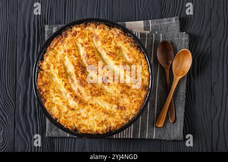 Veganer Hirtenkuchen in Backform auf schwarzem Holztisch mit Holzlöffeln, horizontaler Blick von oben, flach liegend, Nahaufnahme Stockfoto