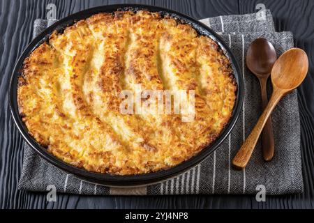 Veganer Hirtenkuchen in Backform auf schwarzem Holztisch mit Löffeln, Landschaftsblick, Nahaufnahme Stockfoto