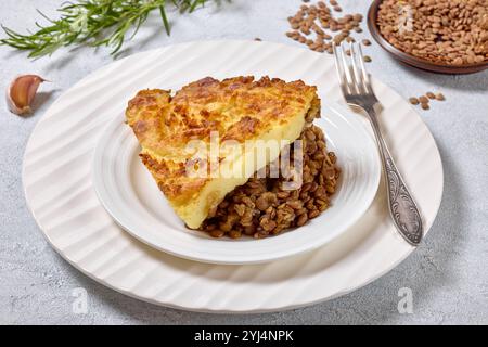 Veganer Hirtenkuchen mit gekochten Linsen, belegt mit Kartoffelpüree auf weißem Teller mit Gabel auf Betontisch, horizontale Ansicht von oben, Nahaufnahme Stockfoto