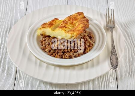 Nahaufnahme von veganen Hirtenkuchen mit gekochten Linsen, belegt mit Kartoffelpüree auf weißem Teller mit Gabel auf Holztisch Stockfoto