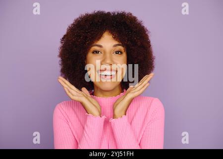 Eine junge afroamerikanische Frau strahlt vor Freude und zeigt ihr lockiges Haar in lässiger rosa Kleidung. Stockfoto