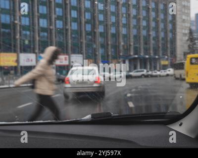 Blick aus der Fahrerkabine auf Fußgänger, die die Straße überqueren, und Autos und Busse, die an einem verschneiten, regnerischen grauen Tag fahren. Gebäude und Reklametafeln hinten Stockfoto