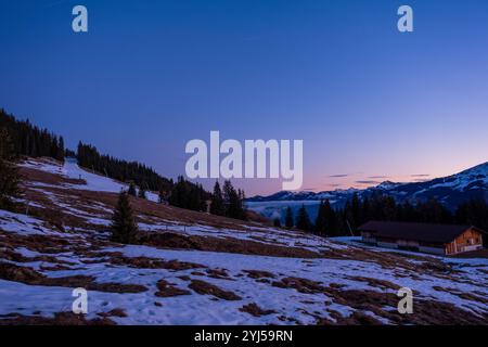 Alpiner Sonnenaufgang auf den Kitzbüheler Alpen mit schmelzenden Schneegebieten und immergrünem Wald. Dramatische Morgenfarben prägen den Himmel über schneebedeckten Berggipfeln. Stockfoto